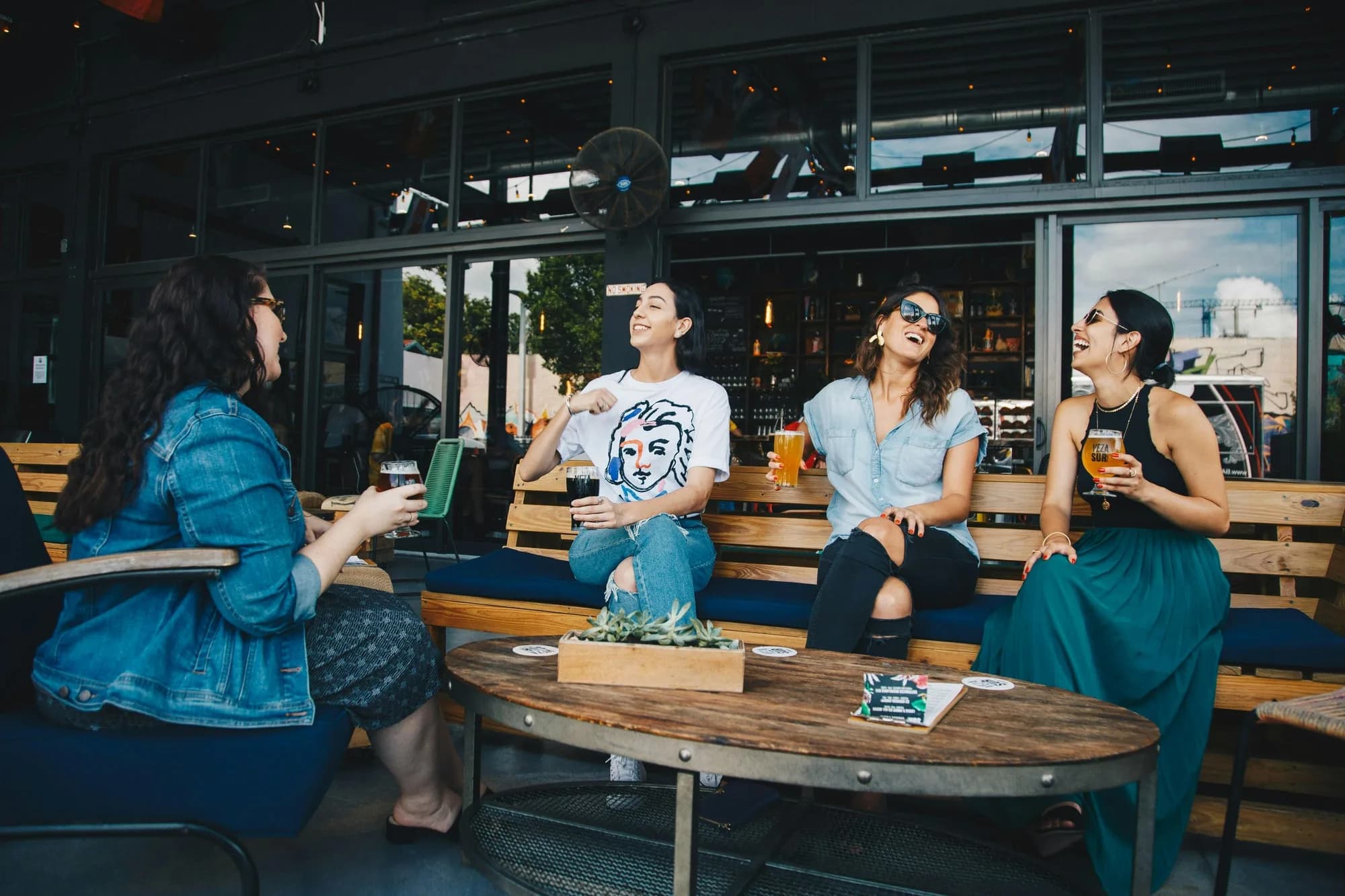 Four friends laughing around a table with drinks