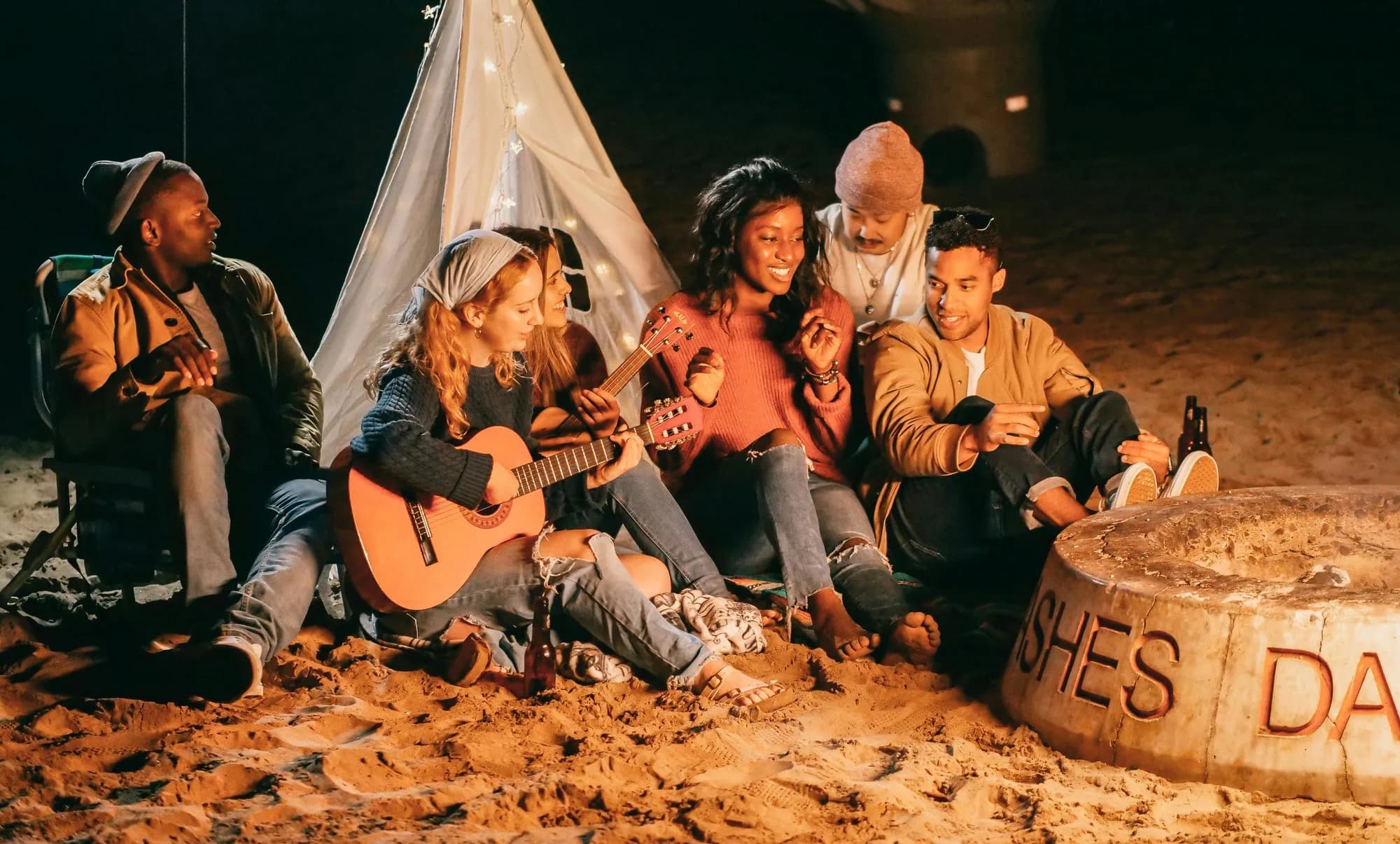 Friends gathered around a fire at night, one playing a guitar
